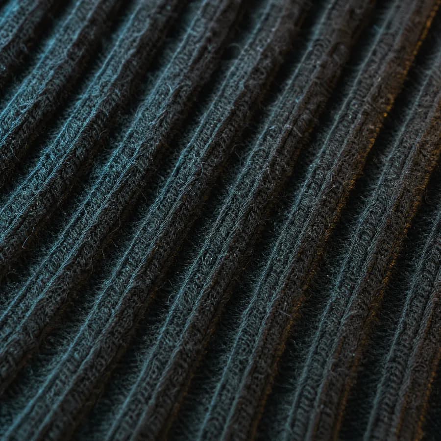 Extreme macro of the ribbed channels of a flat sock cuff, deep parallel grooves in dark yarn