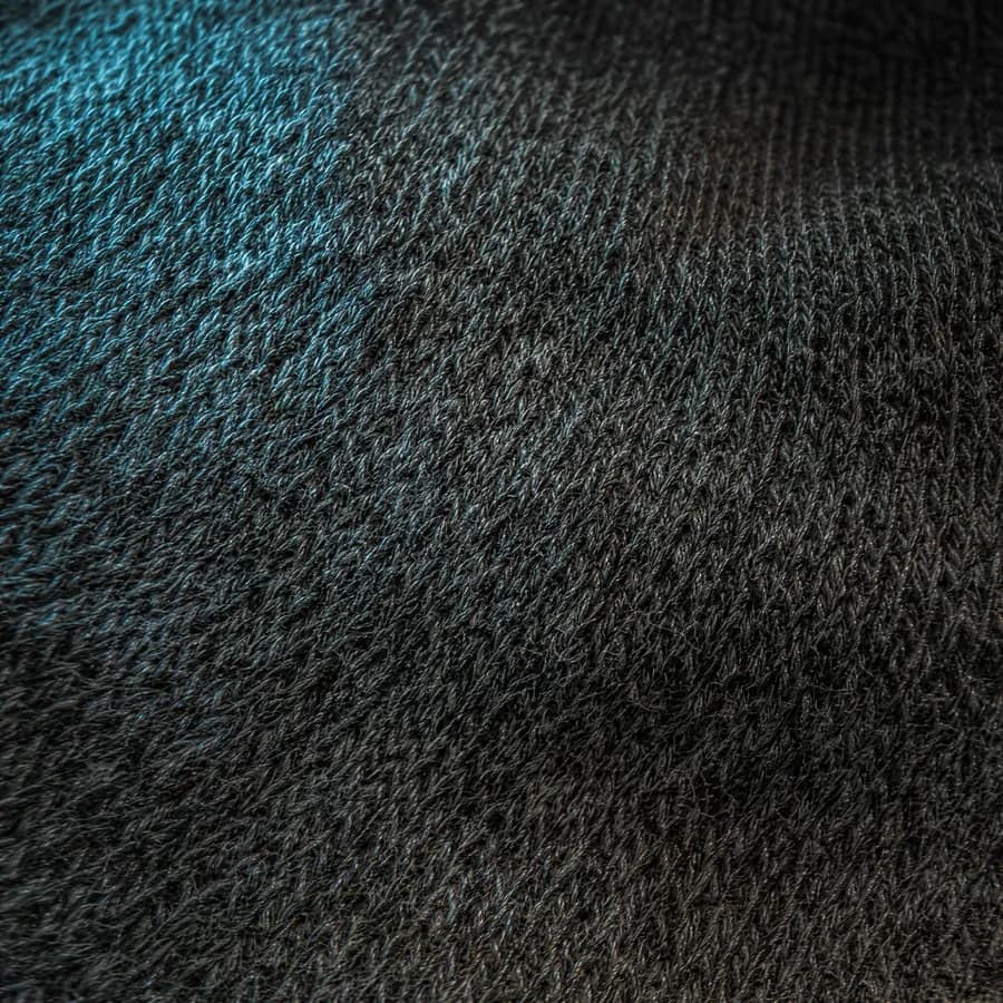 A worn knitted sock heel held over a light panel, the thinned yarn glowing pale where the pile has packed down