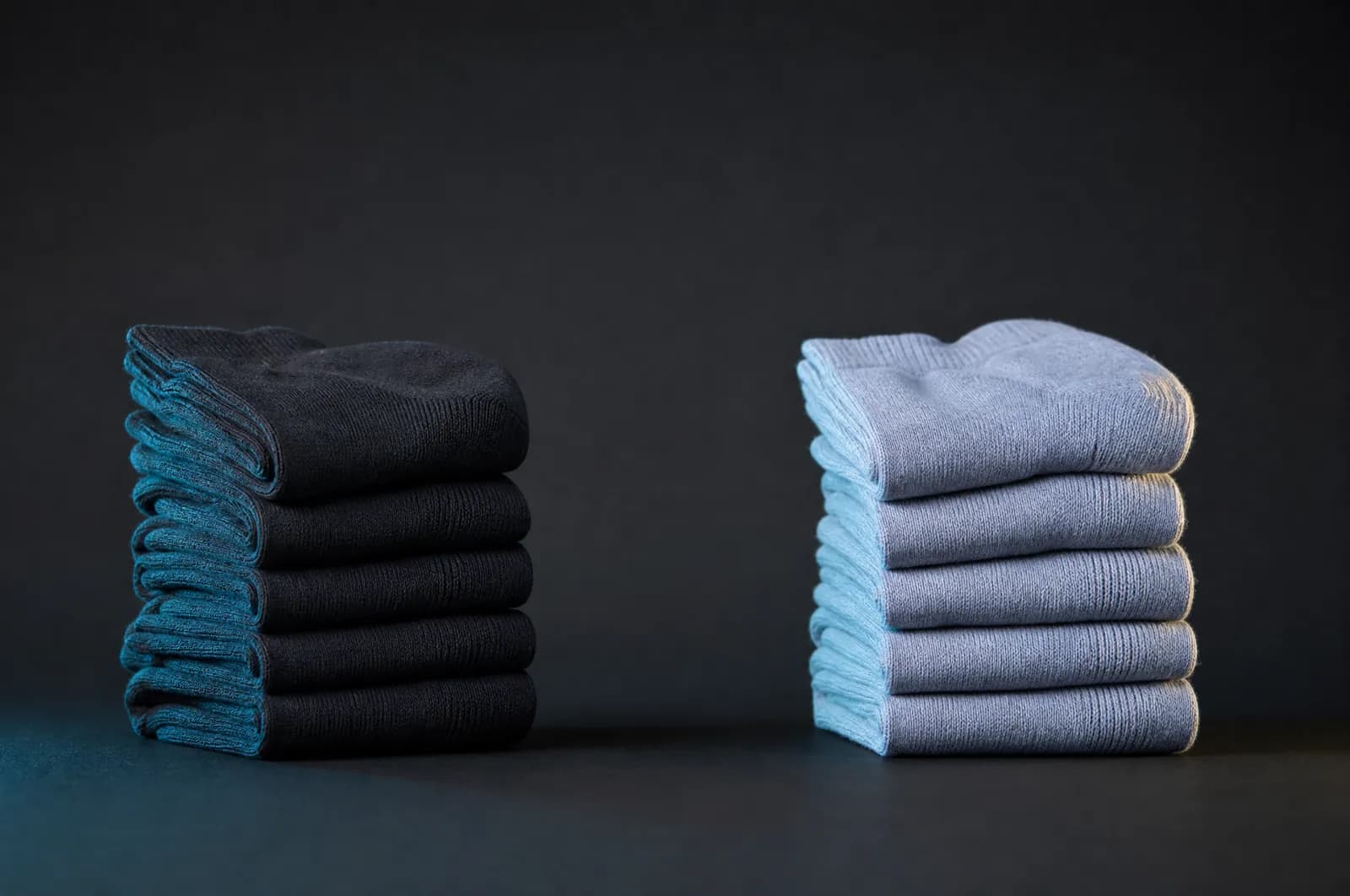 Two separated groups of folded plain socks on a dark bench with a clear gap between them